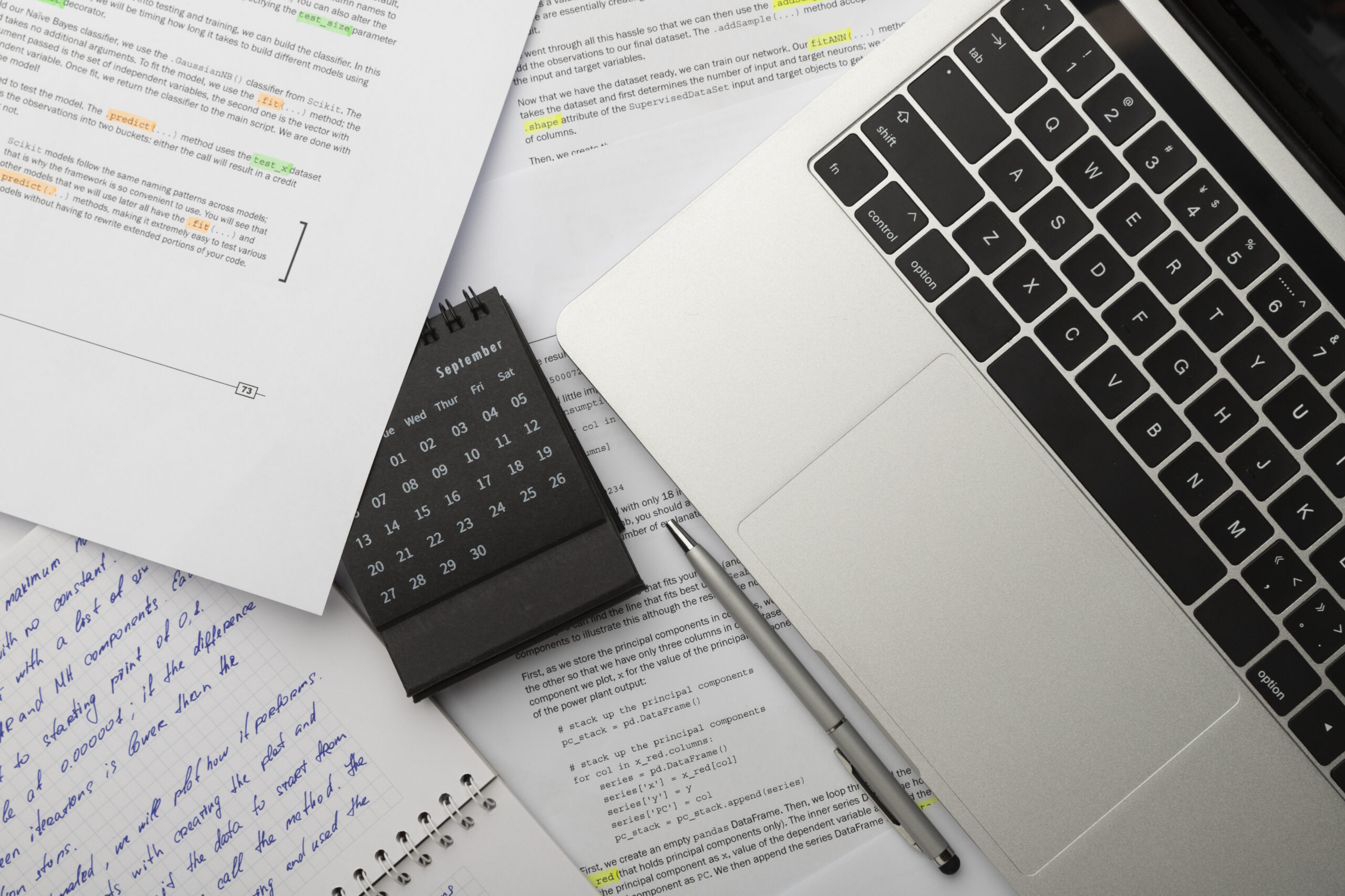 Biurko z otwartym laptopem, ręcznie pisane notatki, wydruki z kodem programowania i kalendarz na wrzesień.