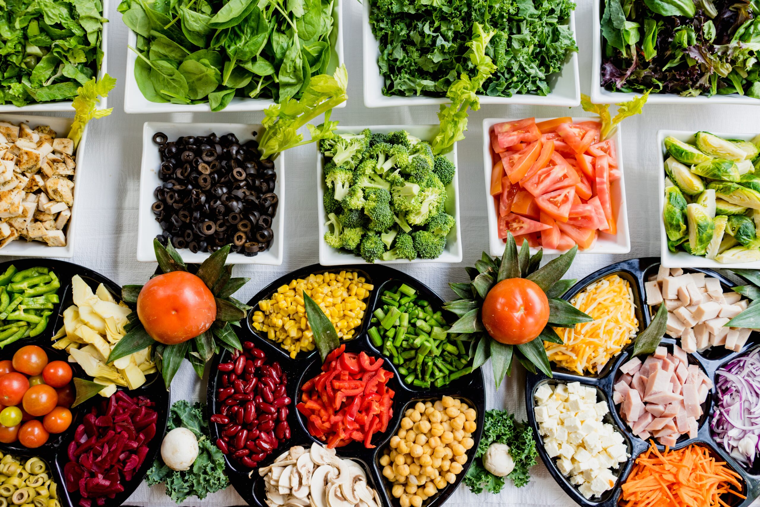 Różnorodność świeżych, kolorowych składników diety śródziemnomorskiej, w tym warzywa liściaste, strączki, oliwki, i pełnoziarniste produkty, pięknie wyłożone na stole.