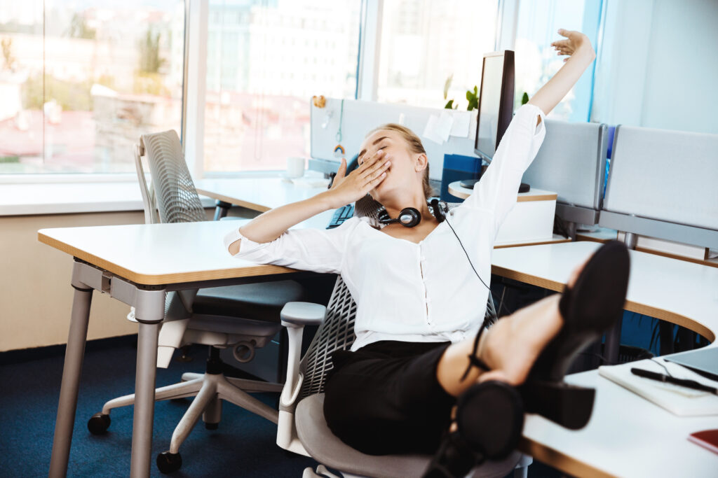 Kobieta pracująca w biurze wykonująca proste ćwiczenia rozciągające przy biurku, relaksując się i odprężając kręgosłup, z nogami wyciągniętymi na drugie krzesło.