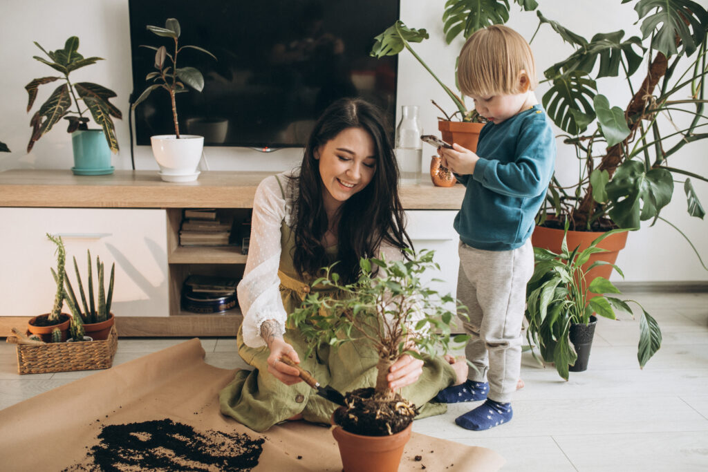 Młoda kobieta i dziecko sadzą roślinę w doniczce w domu pełnym zieleni, wspólnie pielęgnując rodzinne hobby i ucząc o odpowiedzialności oraz przyrodzie.