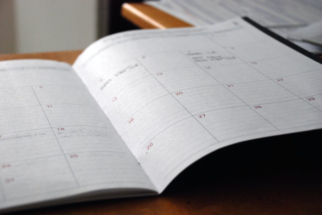 Otwarty terminarz na biurku z zaznaczonymi datami i notatkami, prezentujący dokładne planowanie i organizację obowiązków domowych na każdy dzień miesiąca