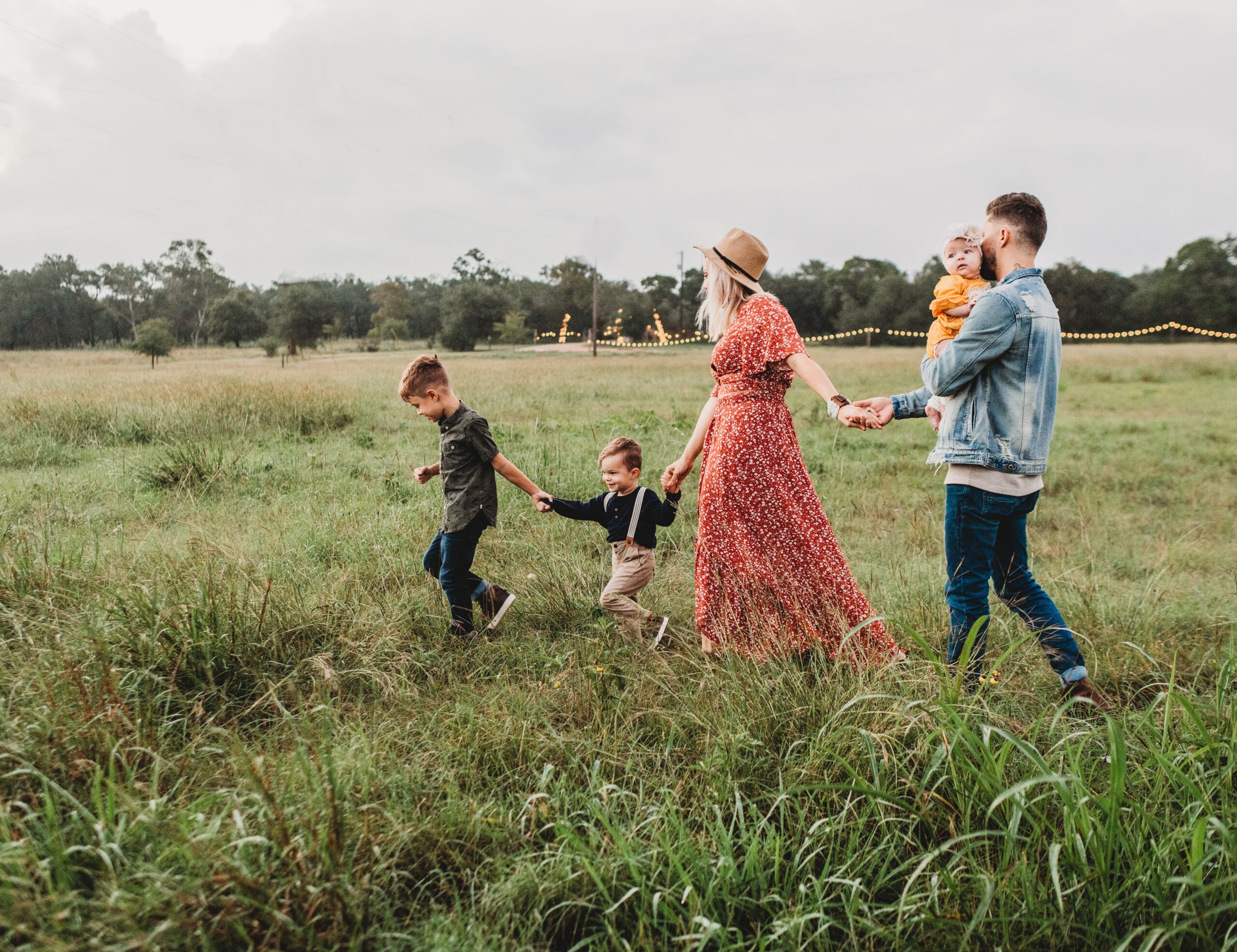Rodzina w radosnym spacerze przez zieloną łąkę, z uśmiechniętymi rodzicami trzymającymi za ręce swoje dzieci, tworzy poczucie jedności i szczęścia na świeżym powietrzu.