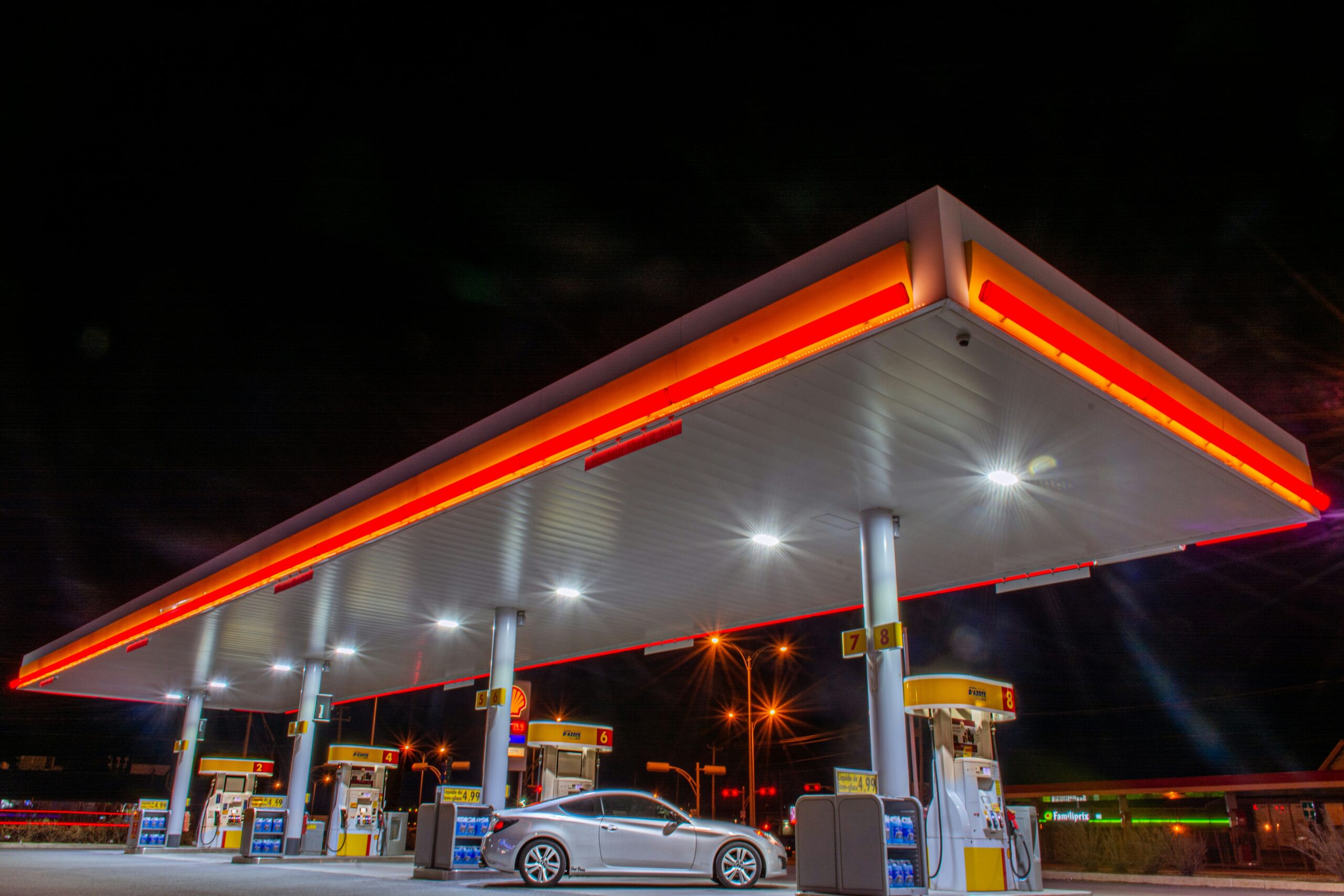 Oświetlona stacja benzynowa nocą, z lśniącymi dystrybutorami paliwa, gotowa na wprowadzenie nowego rodzaju benzyny E10.